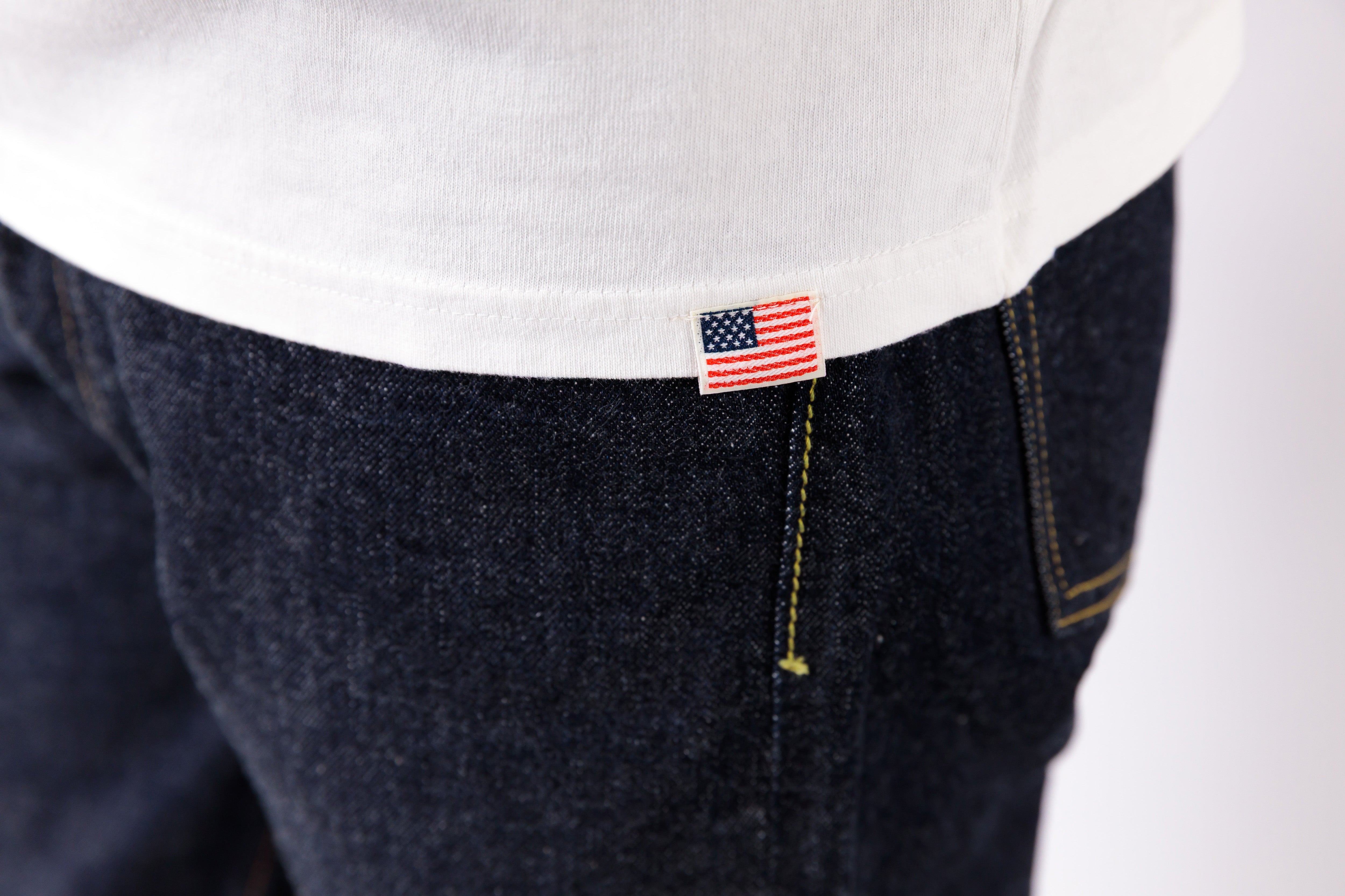 Close-up of a pocket with an American flag pin on dark jeans against a white background