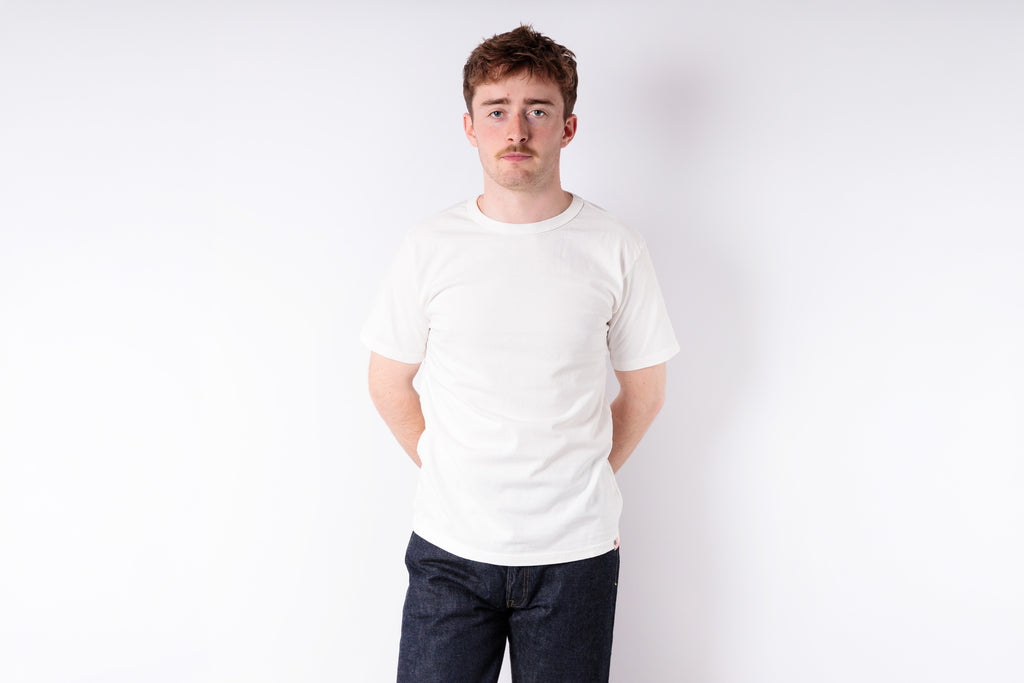 Man wearing a plain white t-shirt and dark pants against a white background