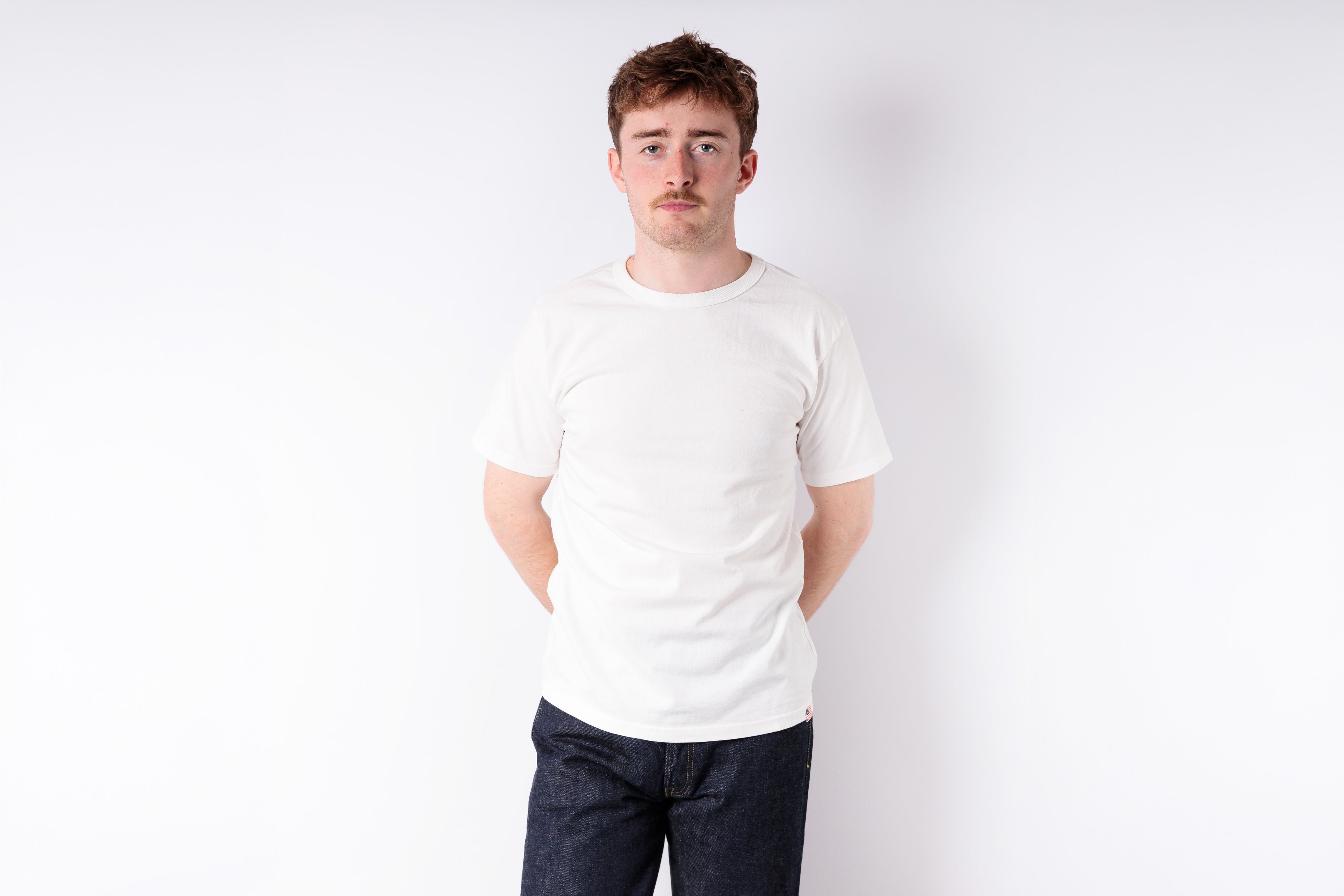 Man wearing a plain white t-shirt and dark pants against a white background