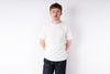 Man wearing a plain white t-shirt and dark pants against a white background