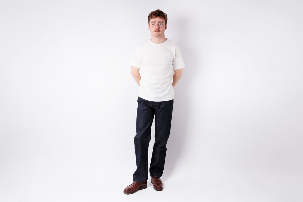 Man wearing a white shirt and dark pants standing against a white background