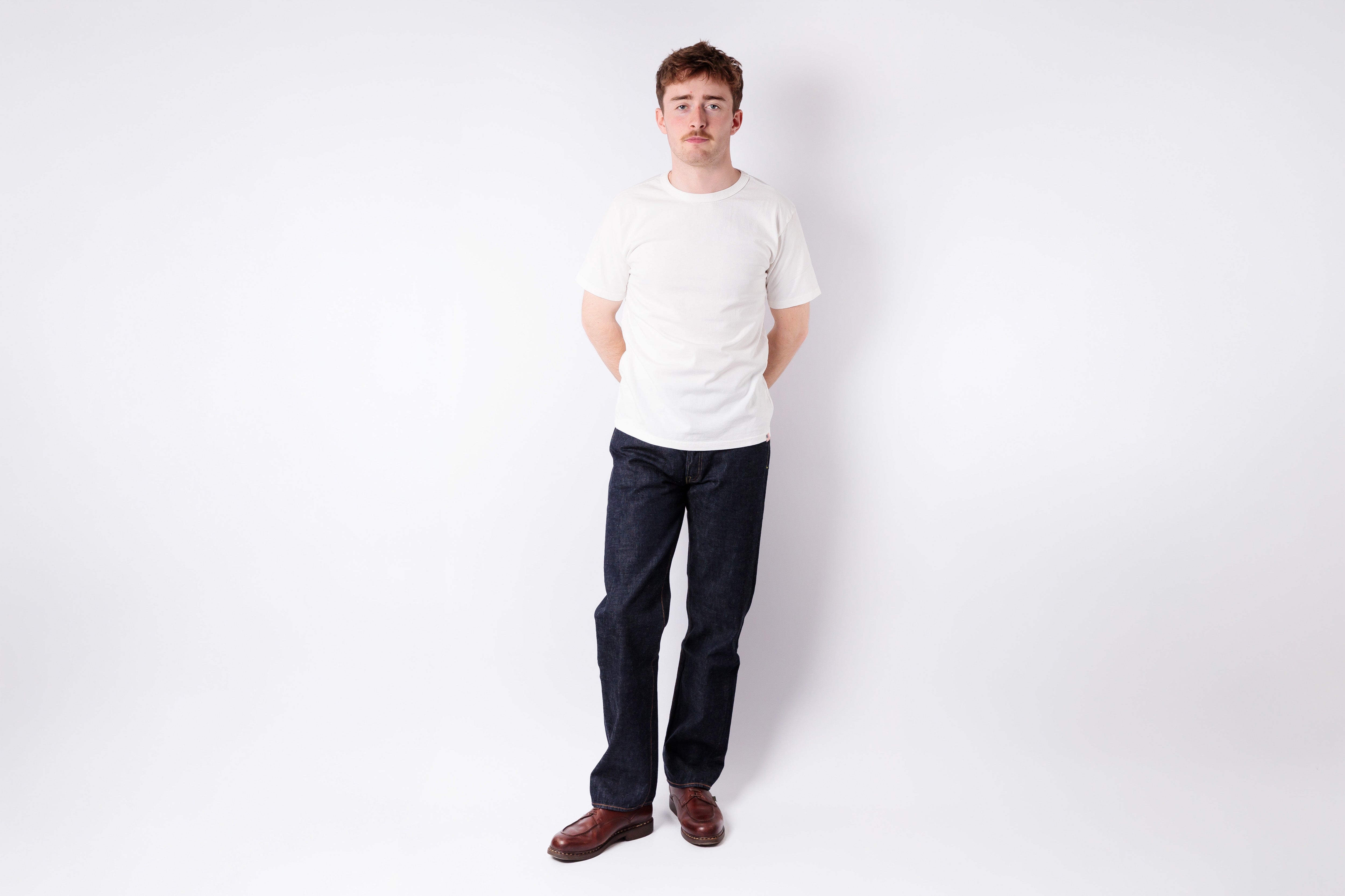 Man wearing a white shirt and dark pants standing against a white background