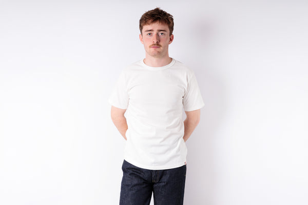 Man wearing a plain white t-shirt and dark pants against a white background