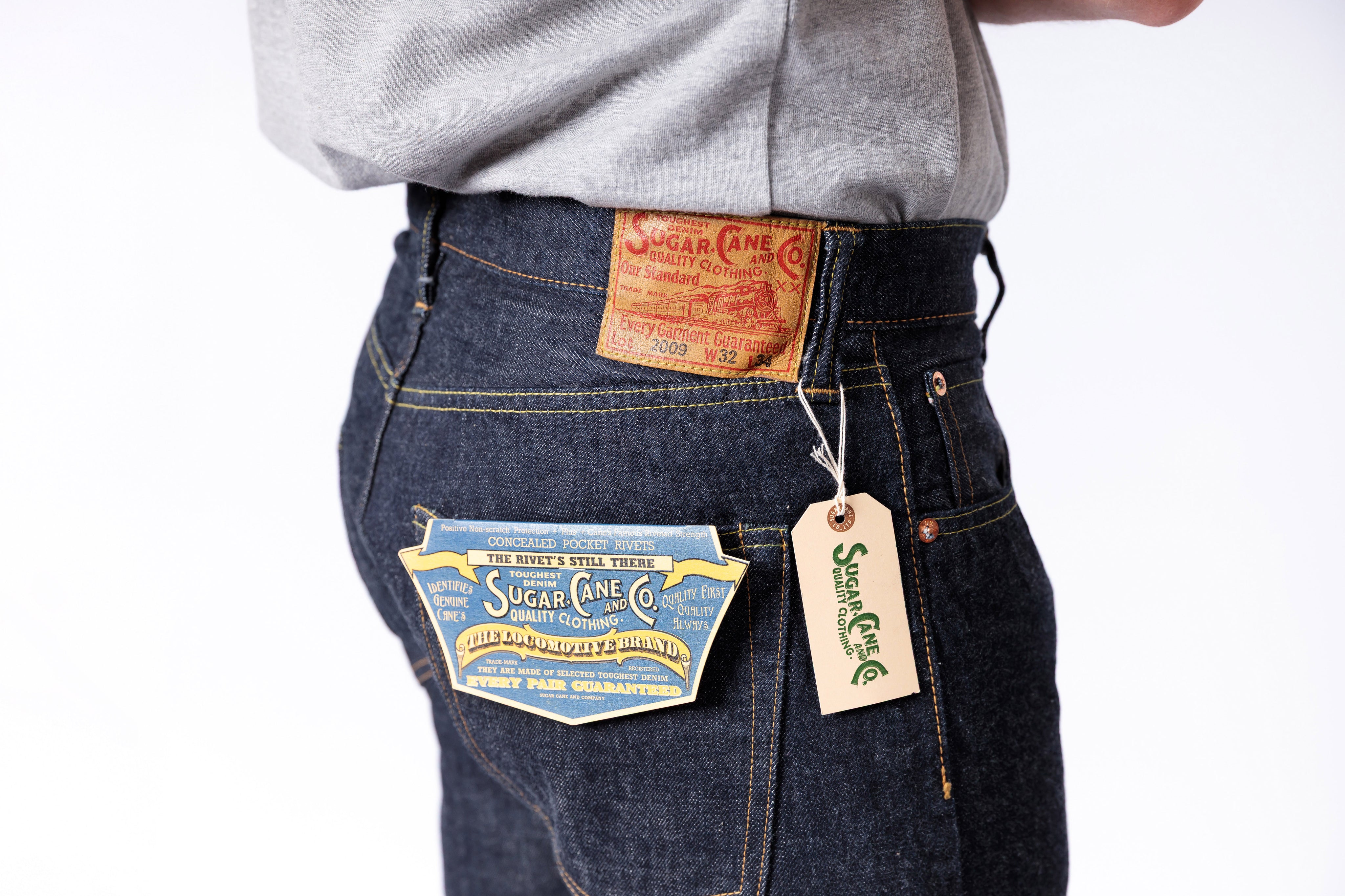 Person wearing dark blue jeans with visible brand labels on a white background