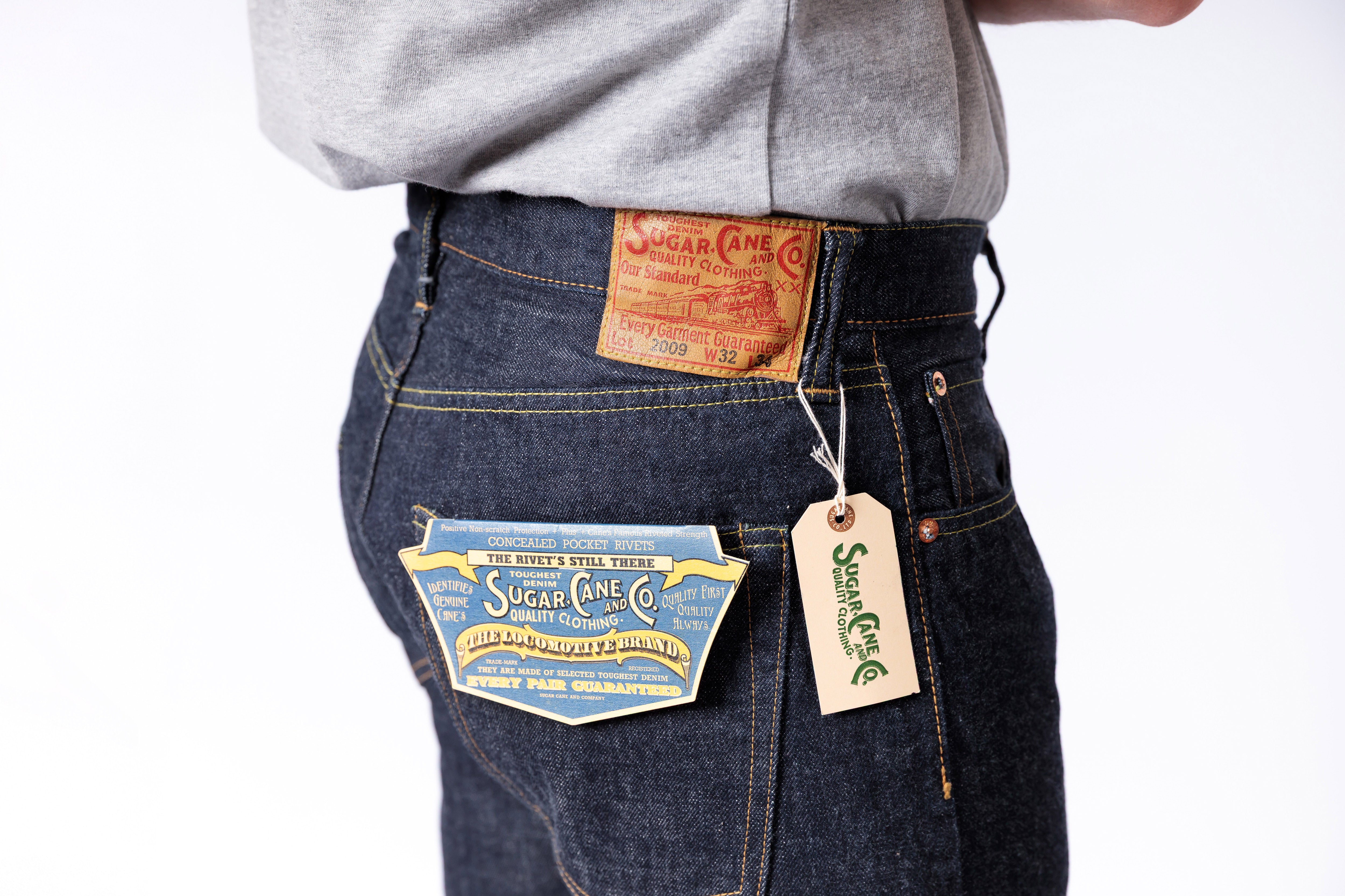 Person wearing dark blue jeans with visible brand labels on a white background