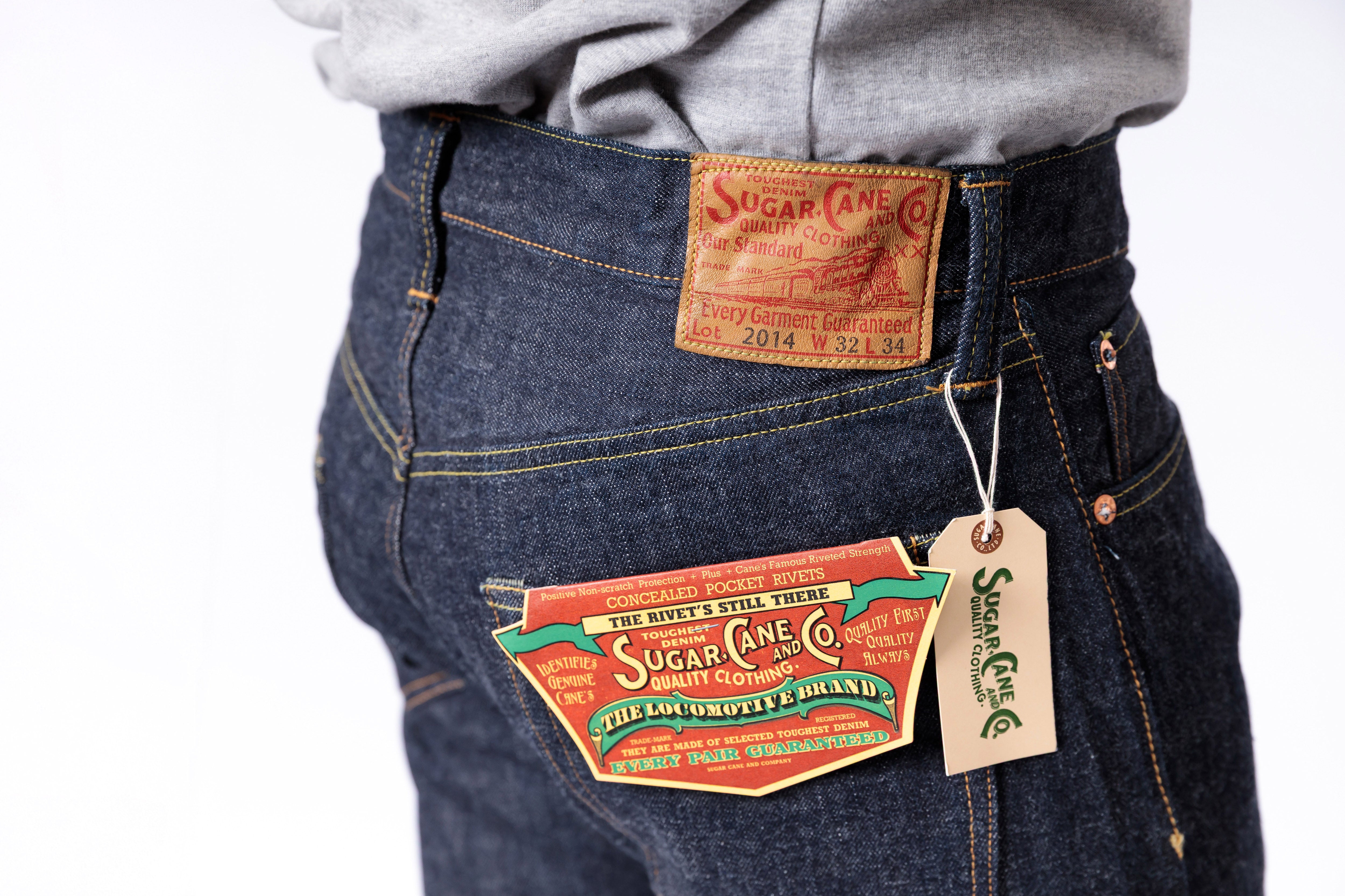 Close-up of a person wearing blue jeans with visible brand labels on a white background