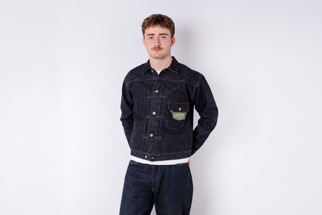 Man wearing a dark denim jacket and pants on a white background