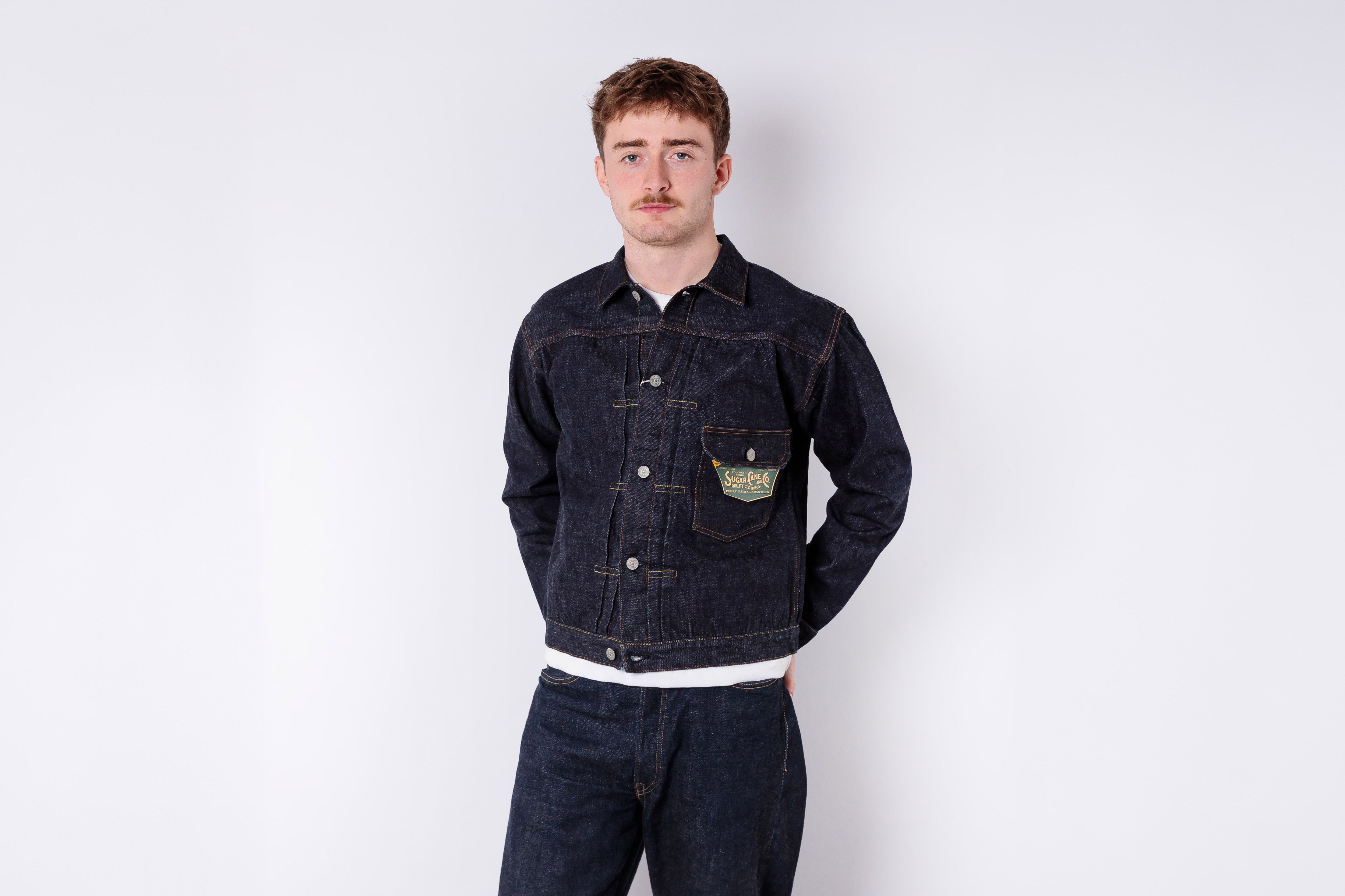 Man wearing a dark denim jacket and pants on a white background