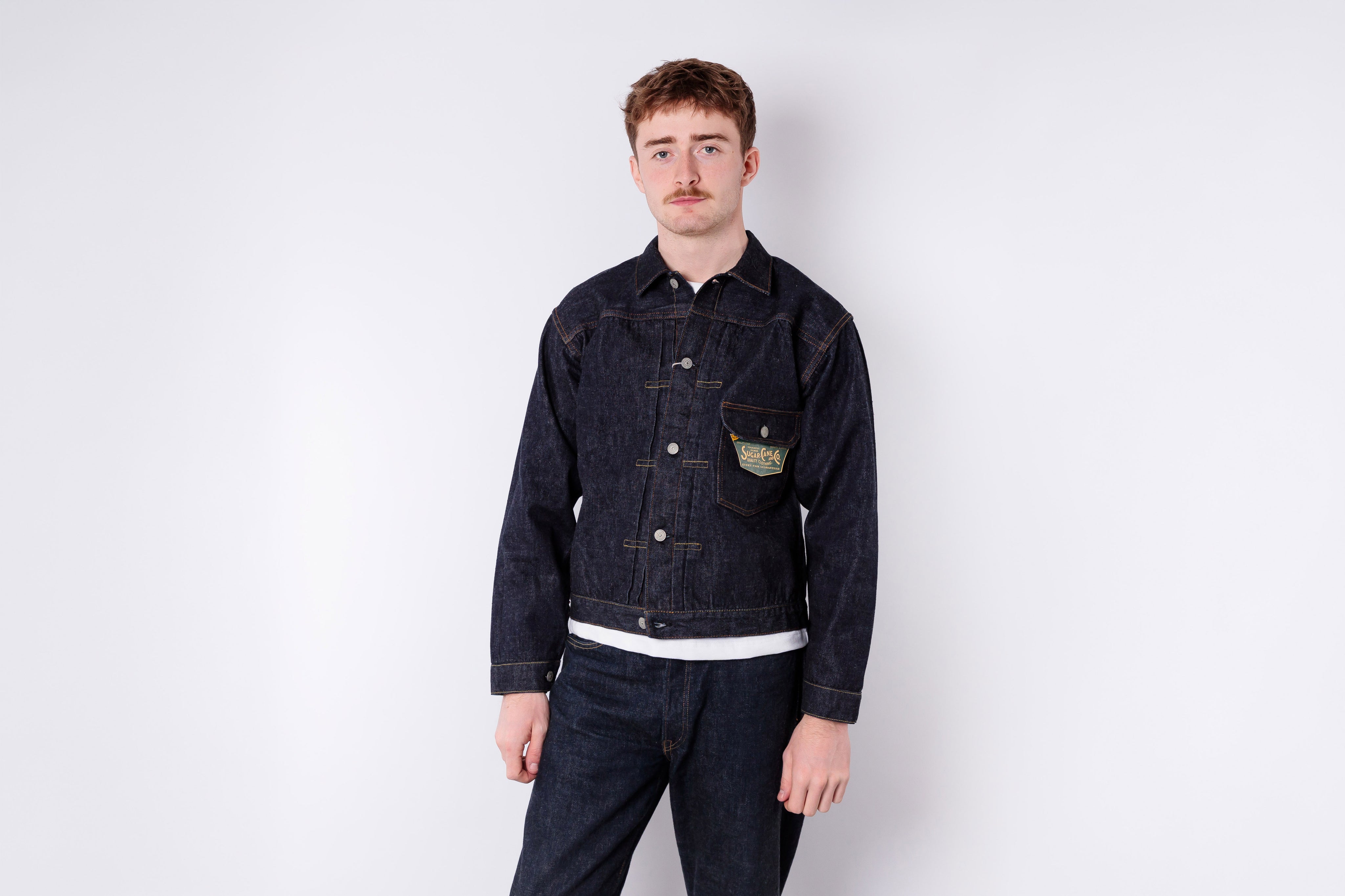 Man wearing a dark denim jacket and pants on a white background