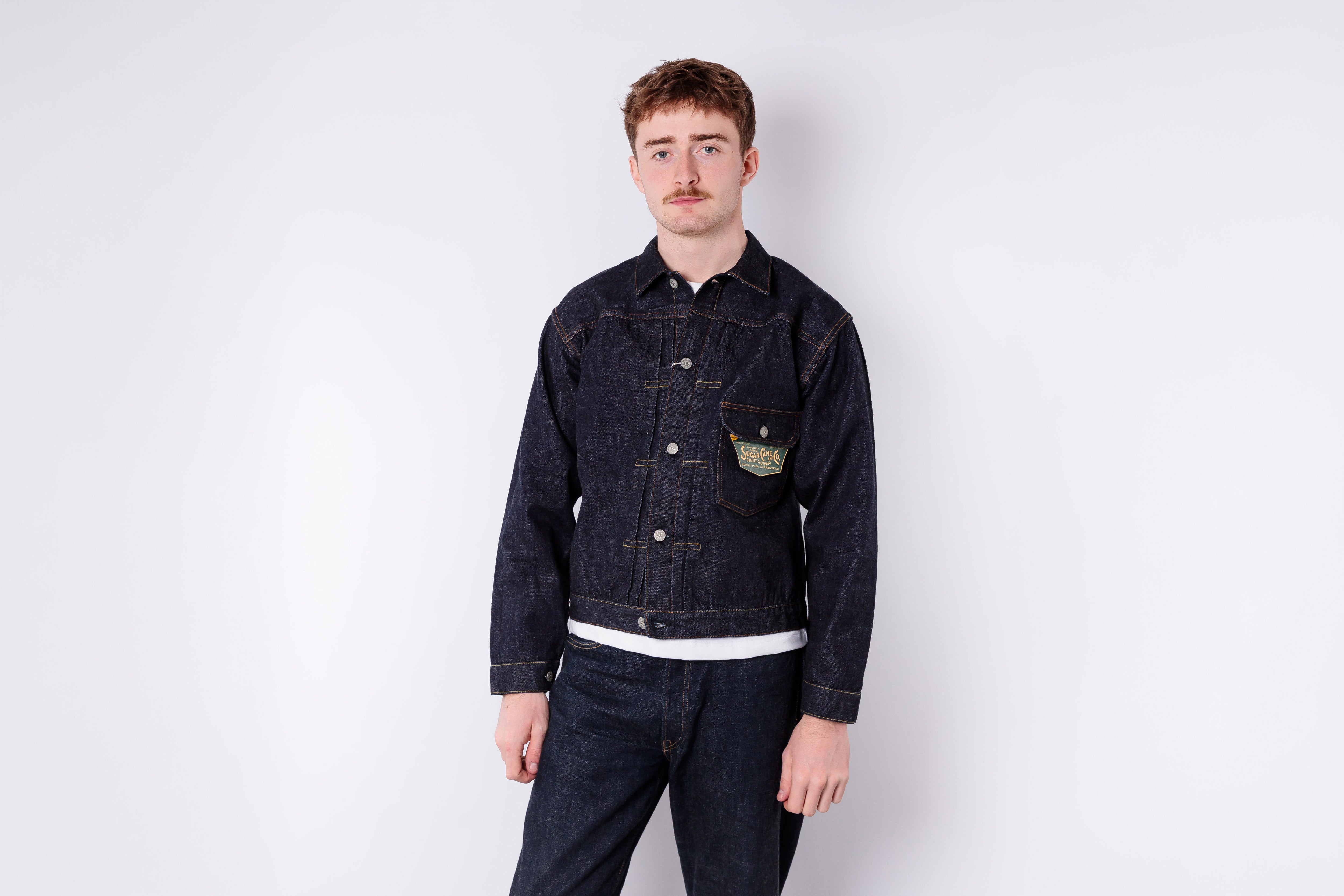 Man wearing a dark denim jacket and pants on a white background
