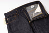 Close-up of dark indigo denim jeans laid flat on a white background, showing the waistband, front pocket, button, zipper, and interior label.