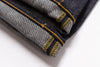 Close-up of folded dark indigo denim jeans showing the twill fabric texture and bright yellow contrast stitching on a white background.