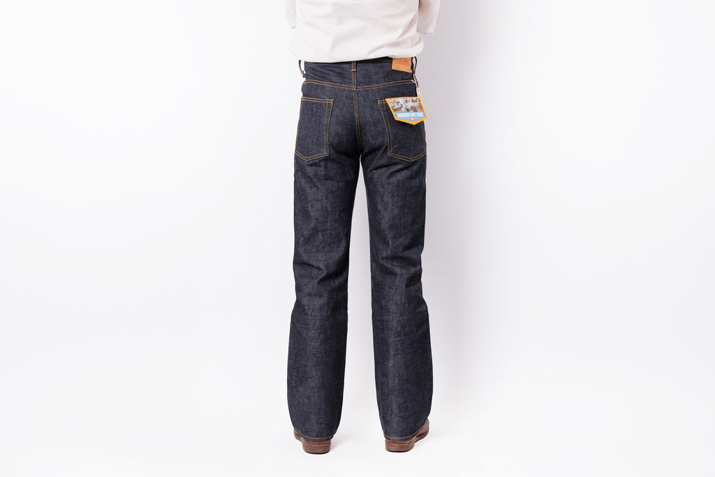 Rear view of a person wearing dark indigo denim jeans with a white shirt, shown against a plain white studio background.