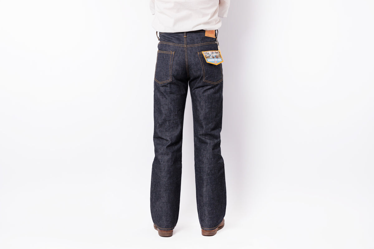 Rear view of a person wearing dark indigo denim jeans with a white shirt, shown against a plain white studio background.