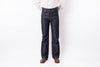 A person wearing dark indigo denim jeans, a white button-down shirt, and brown leather shoes, standing against a plain white studio background.