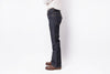 A person shown from the waist down wearing dark indigo flare jeans, a white shirt, and brown leather shoes, standing against a plain white studio background.