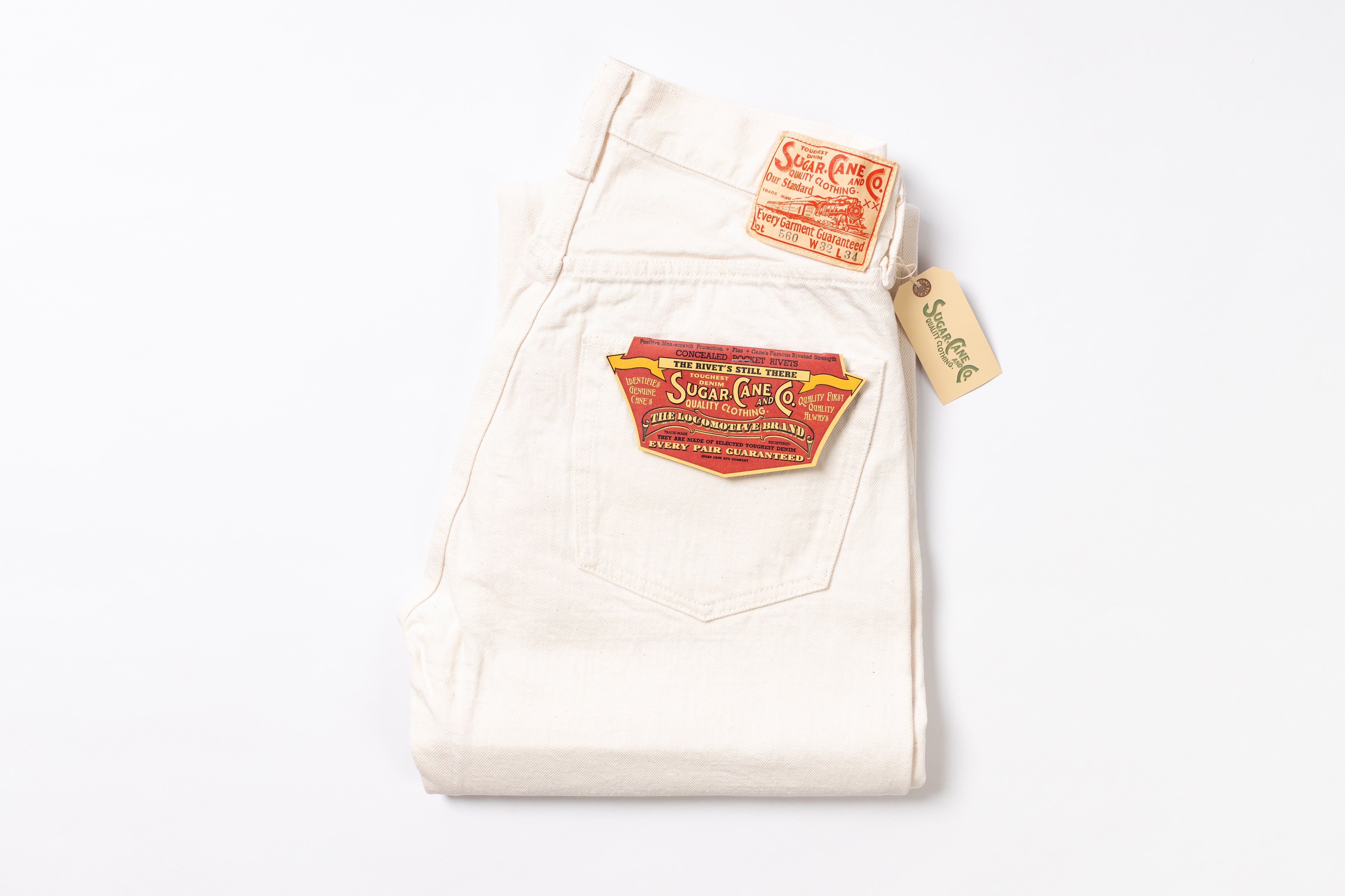 A pair of folded off-white denim jeans with vintage red and yellow patches on the back pocket and a matching paper hangtag, photographed on a clean white background.