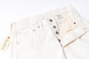 A close-up of off-white denim jeans laid flat on a white background, showing the waistband, button fly, front pockets, and a hanging tag with  branding.