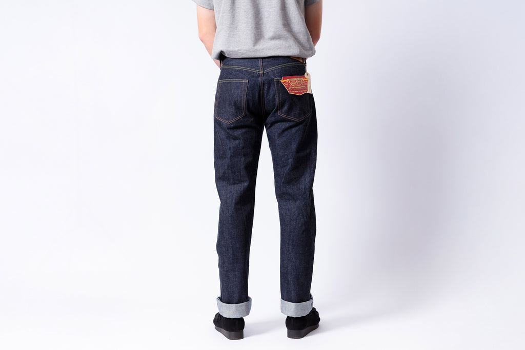 Person wearing dark blue jeans with a visible brand patch on a white background