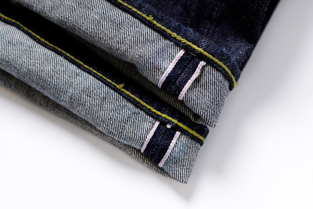 Close-up of folded denim fabric with yellow and white stitching on a white background
