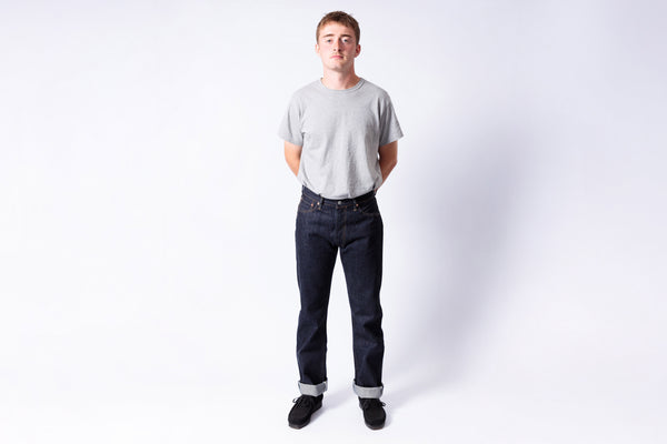 Person wearing a plain gray t-shirt and dark jeans on a white background