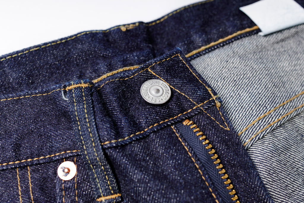 Close-up of a button on a pair of blue jeans with a white background.