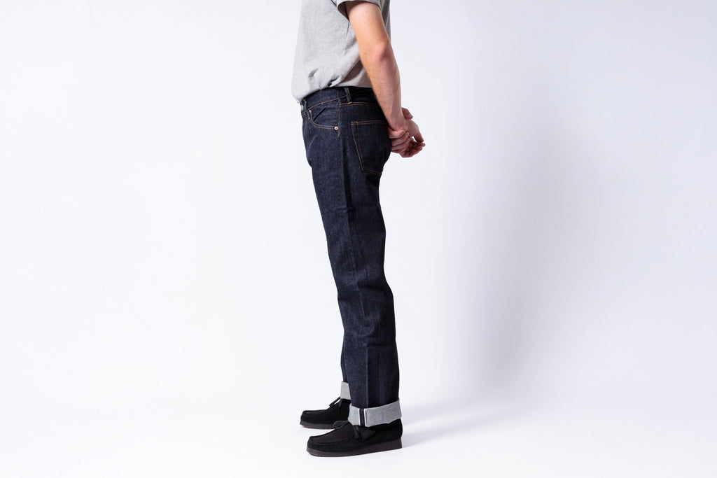 Person wearing dark blue jeans and black shoes on a white background