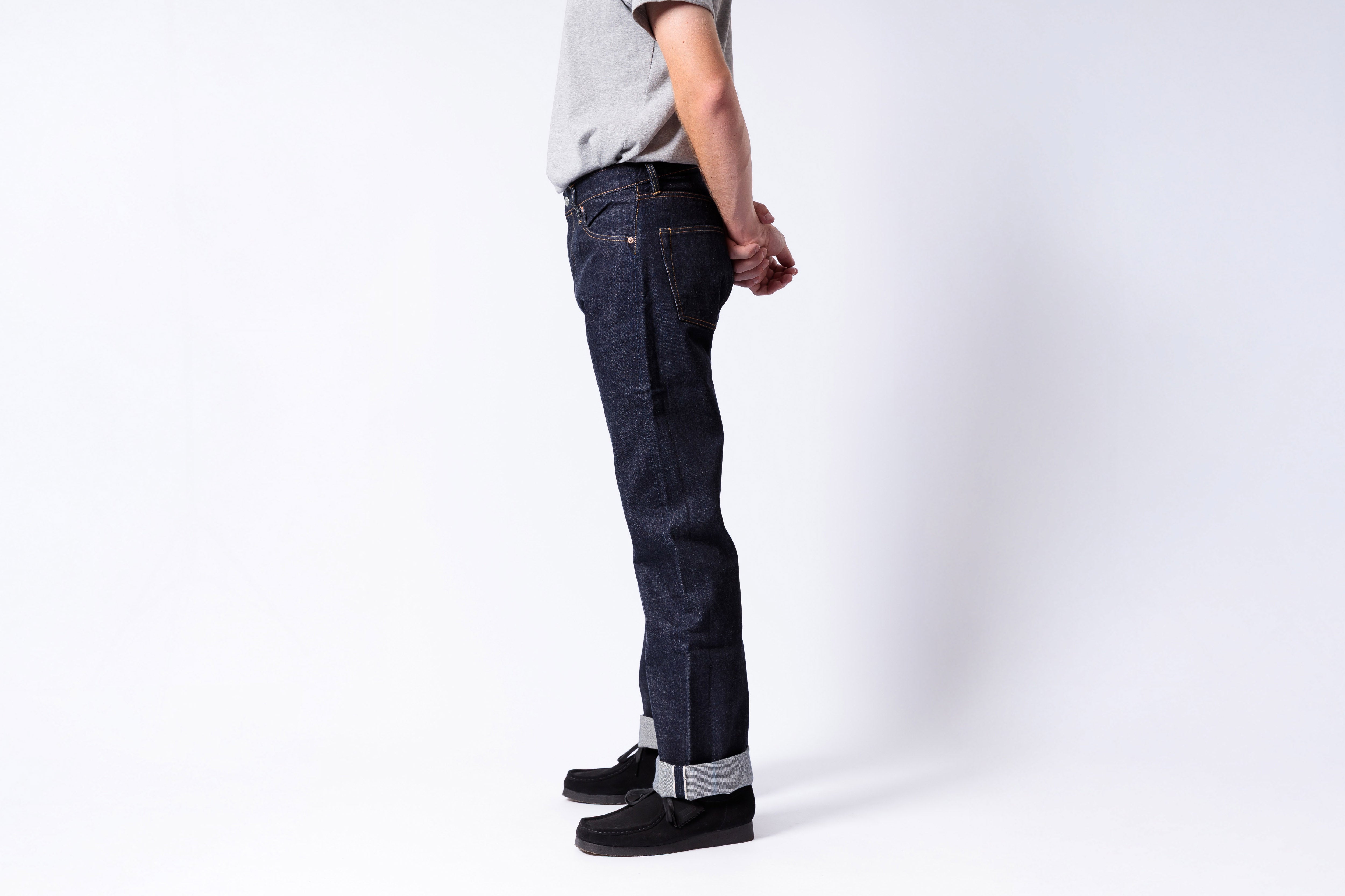 Person wearing dark blue jeans and black shoes on a white background