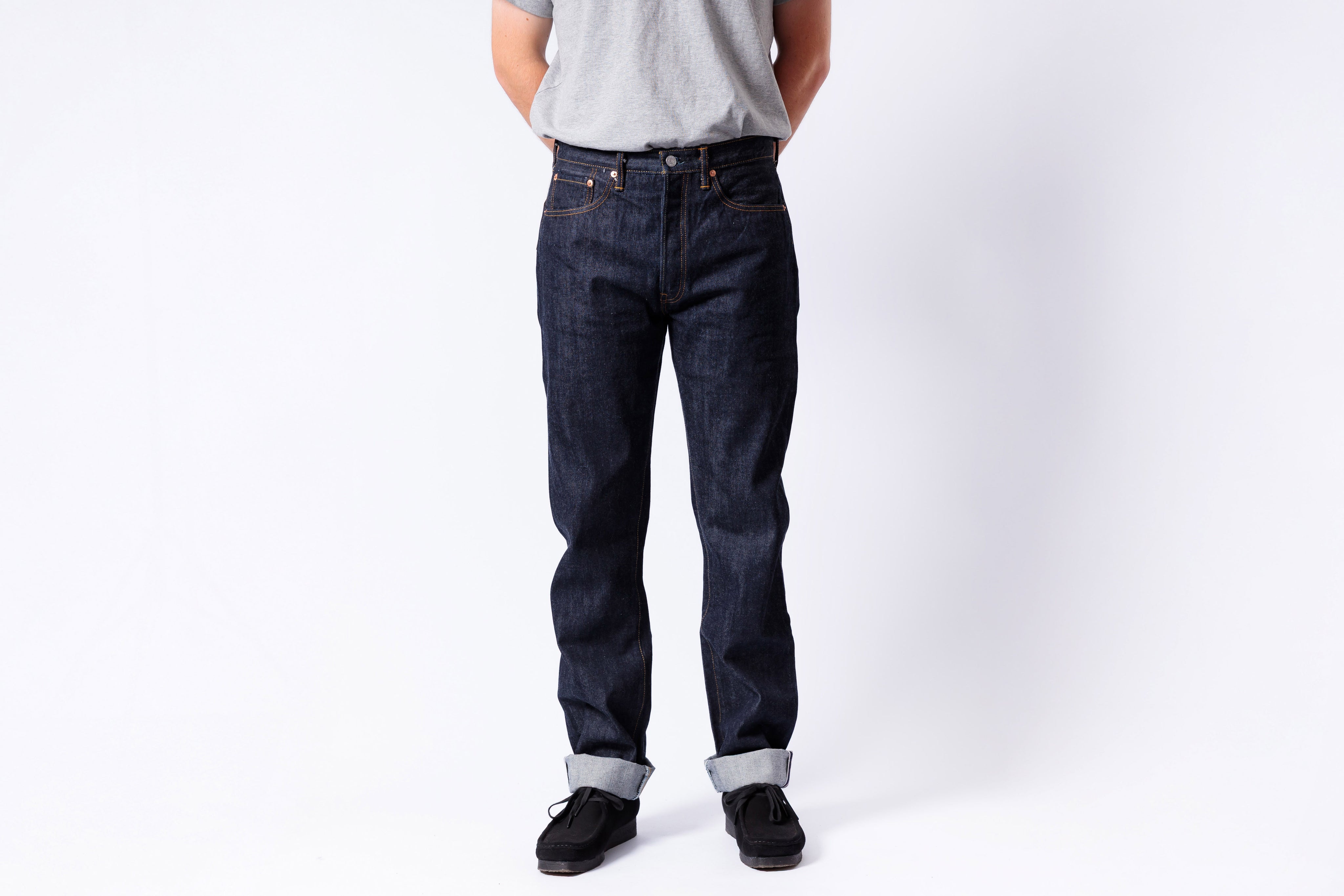 Person wearing dark blue jeans and a light gray shirt on a white background