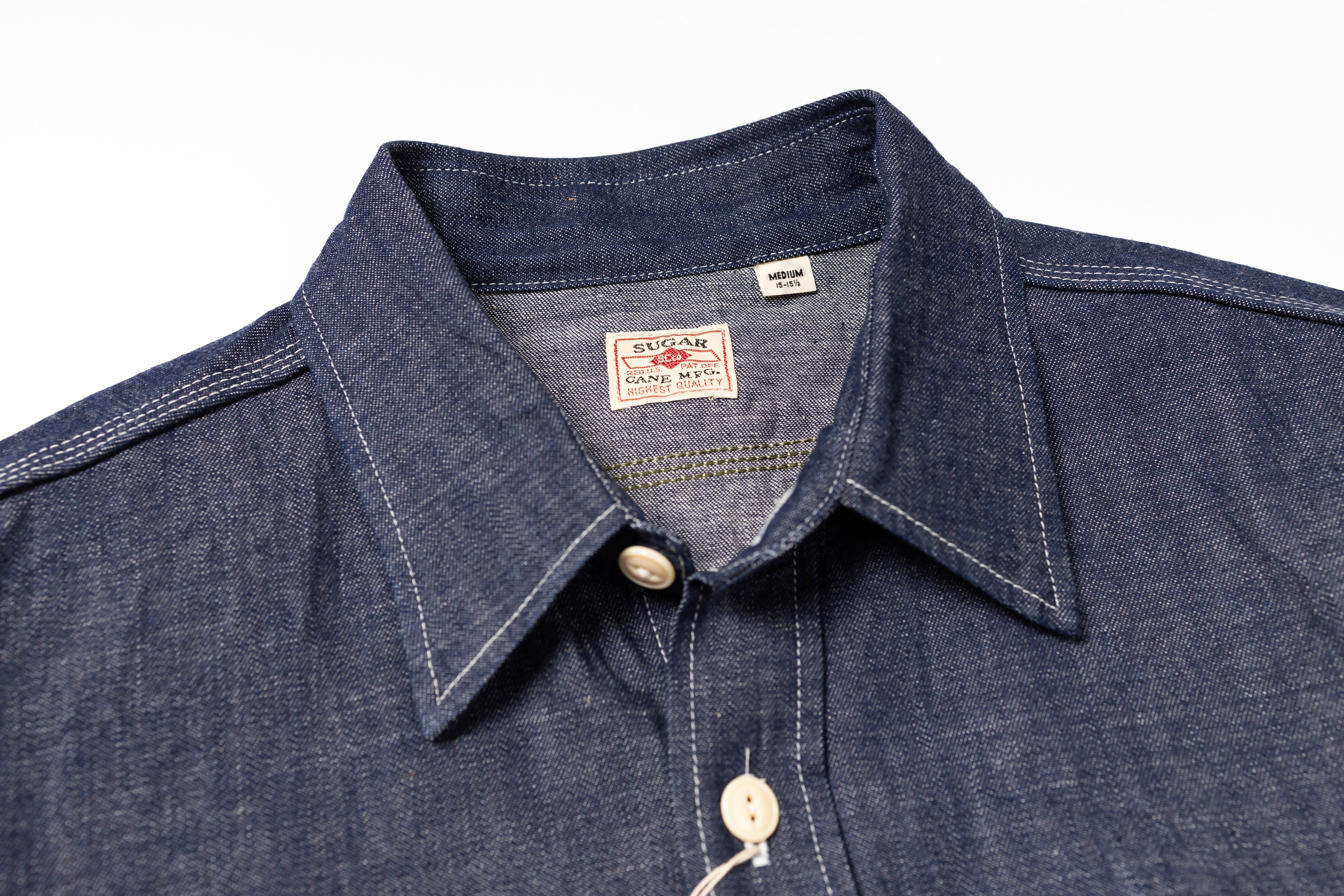 Close-up of a blue denim shirt with collar and brand label on a white background