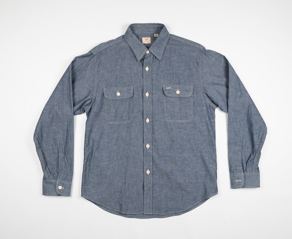A long-sleeved chambray work shirt in indigo color, button-up front, collar, and two chest pockets.