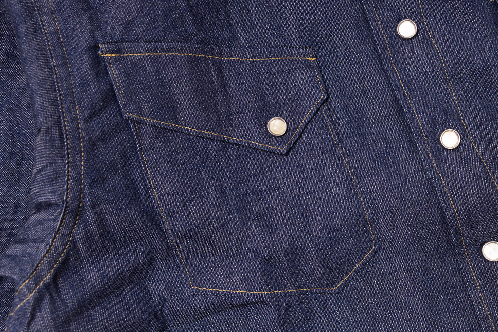 Close-up of a blue denim shirt with a pocket and buttons.