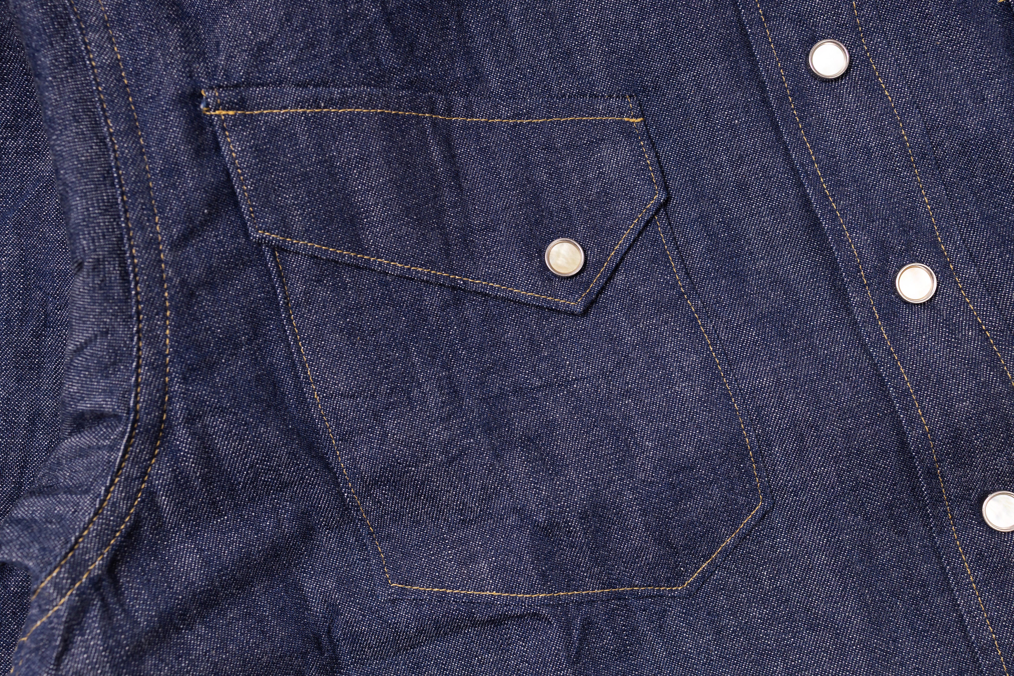 Close-up of a blue denim shirt with a pocket and buttons.