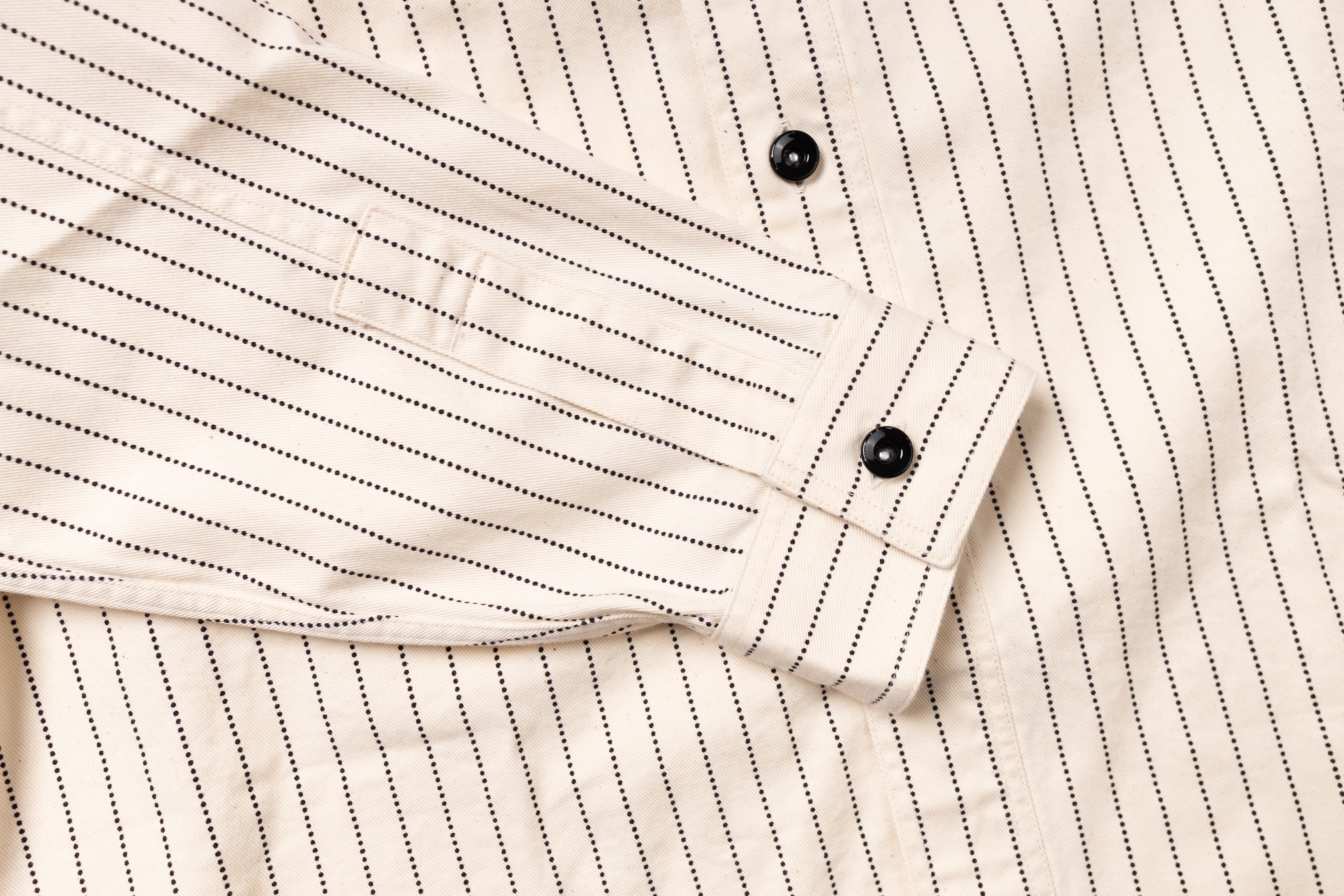 Close-up of a beige pinstripe shirt with black buttons