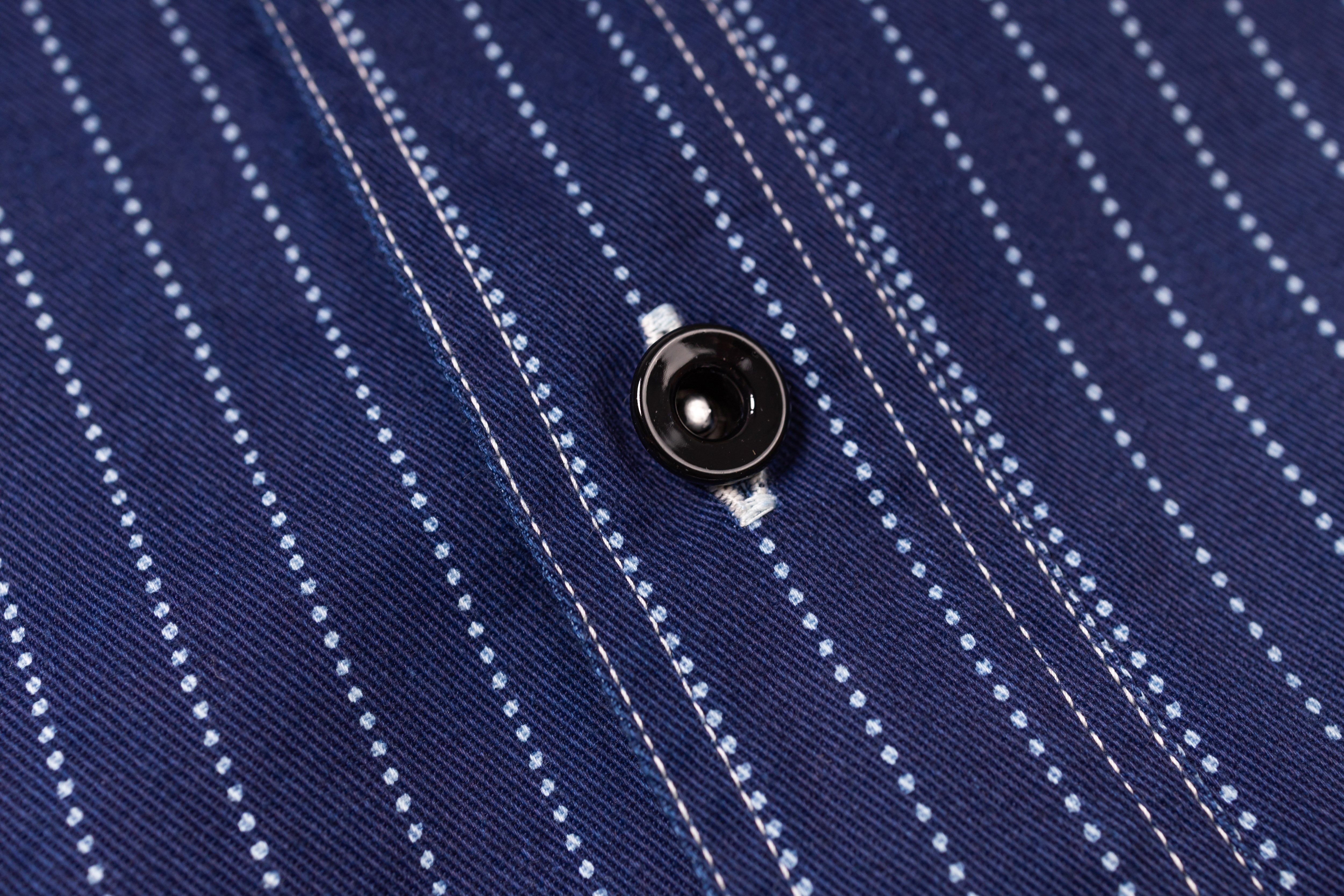 Close-up of a navy blue pinstripe shirt with a button.