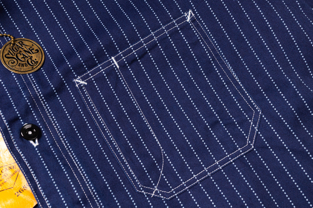 Close-up of a blue pinstripe shirt with a brand logo on a yellow background