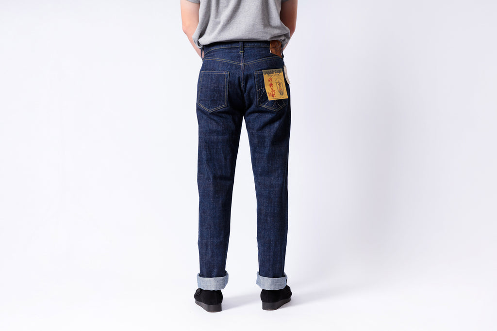 Person wearing blue jeans with a visible brand label on a white background