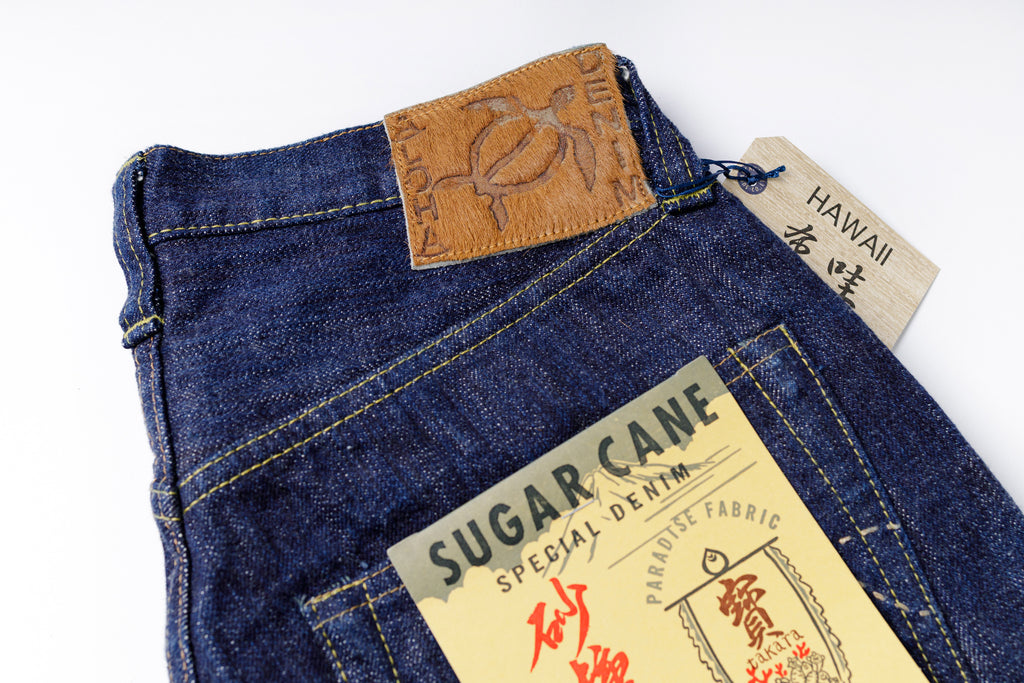 Folded blue denim jeans with a 'Sugar Cane' label on a white background