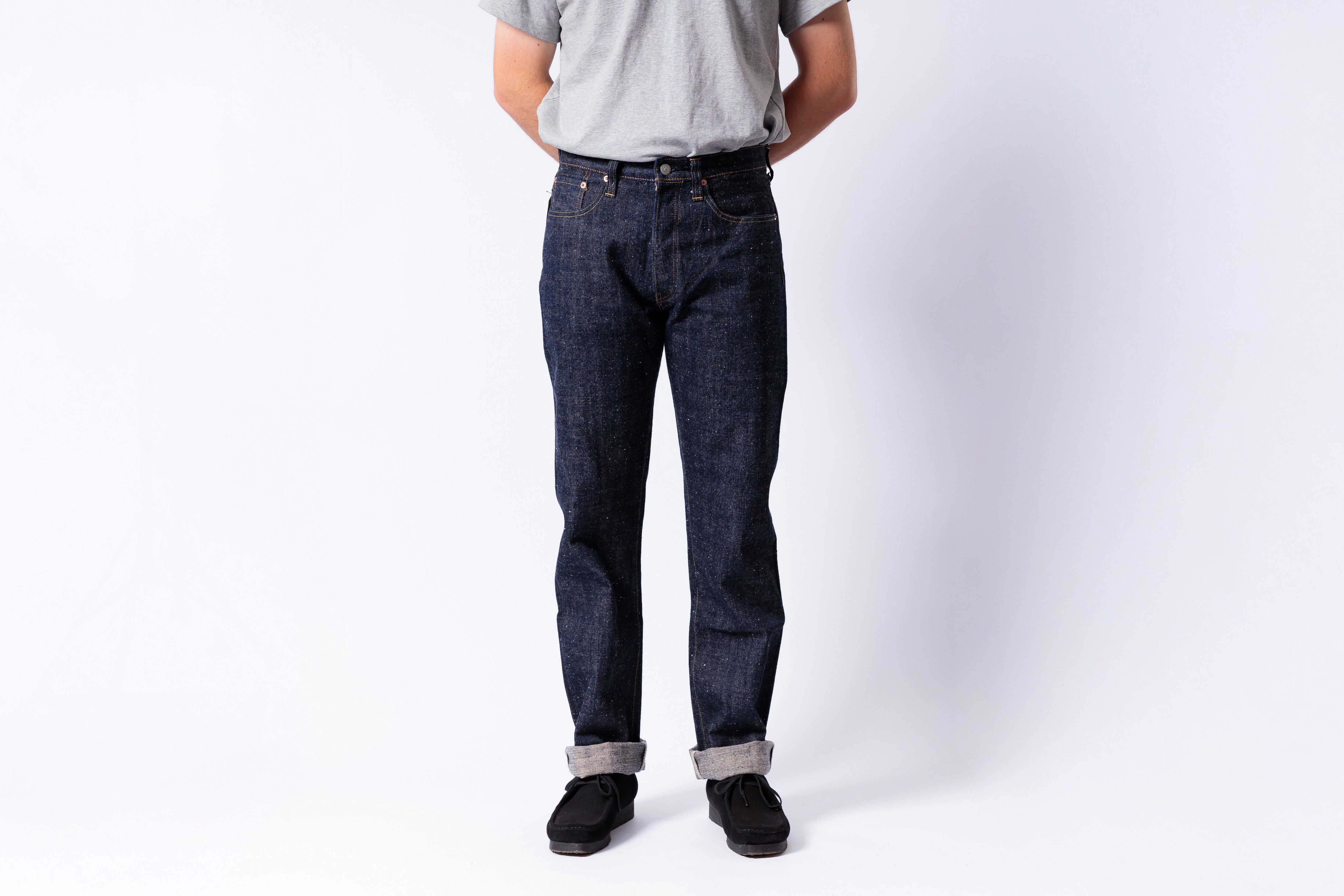 Person wearing dark blue jeans and a gray shirt on a white background