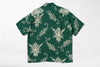 A green short-sleeve button-up shirt with a repeating cream-colored tattoo-style dragon and floral pattern, laid flat against a white background.