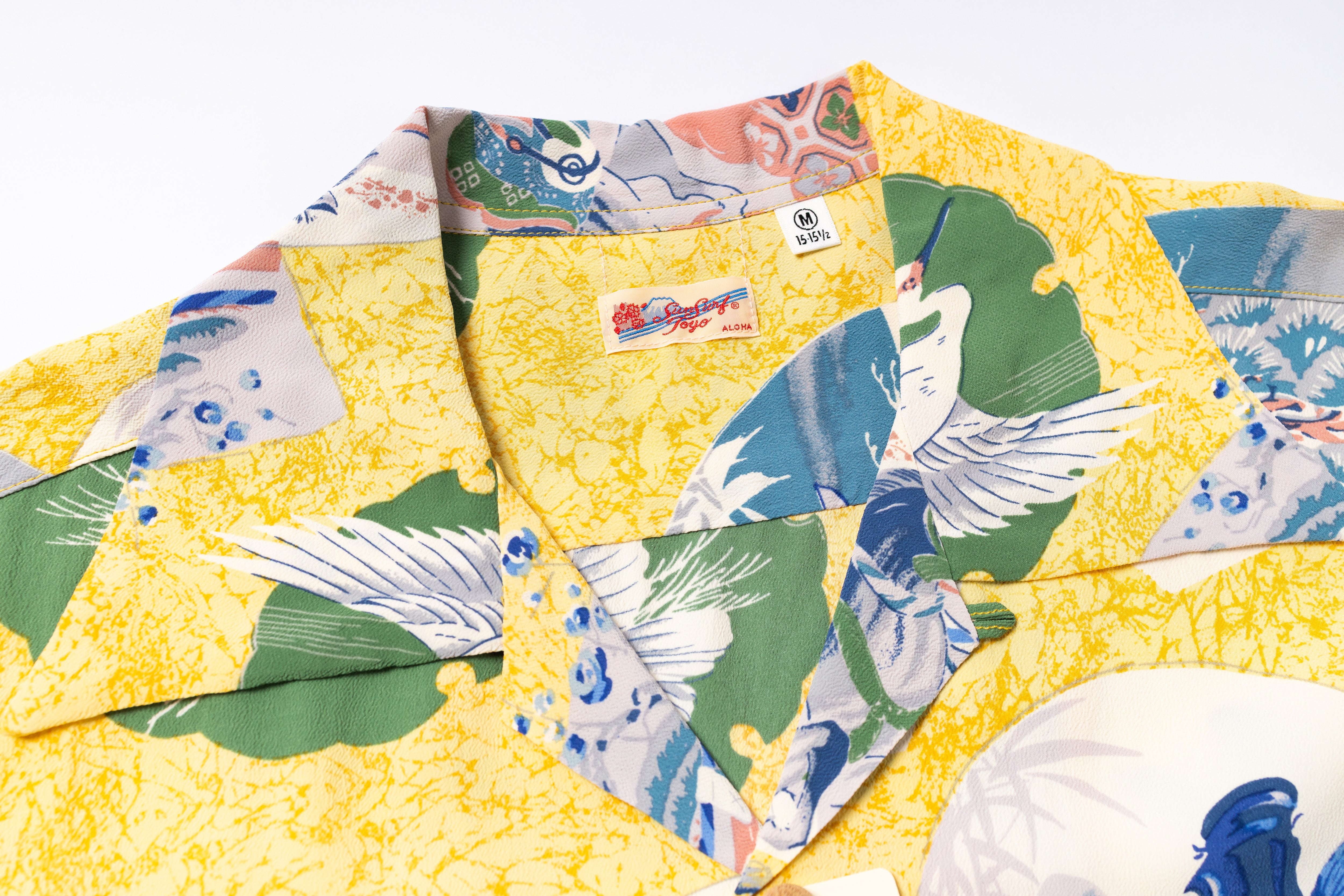A close-up of a yellow short-sleeve camp collar shirt with a Japanese-style crane print in green, blue, and white, featuring a visible 'Sun Surf' brand label.