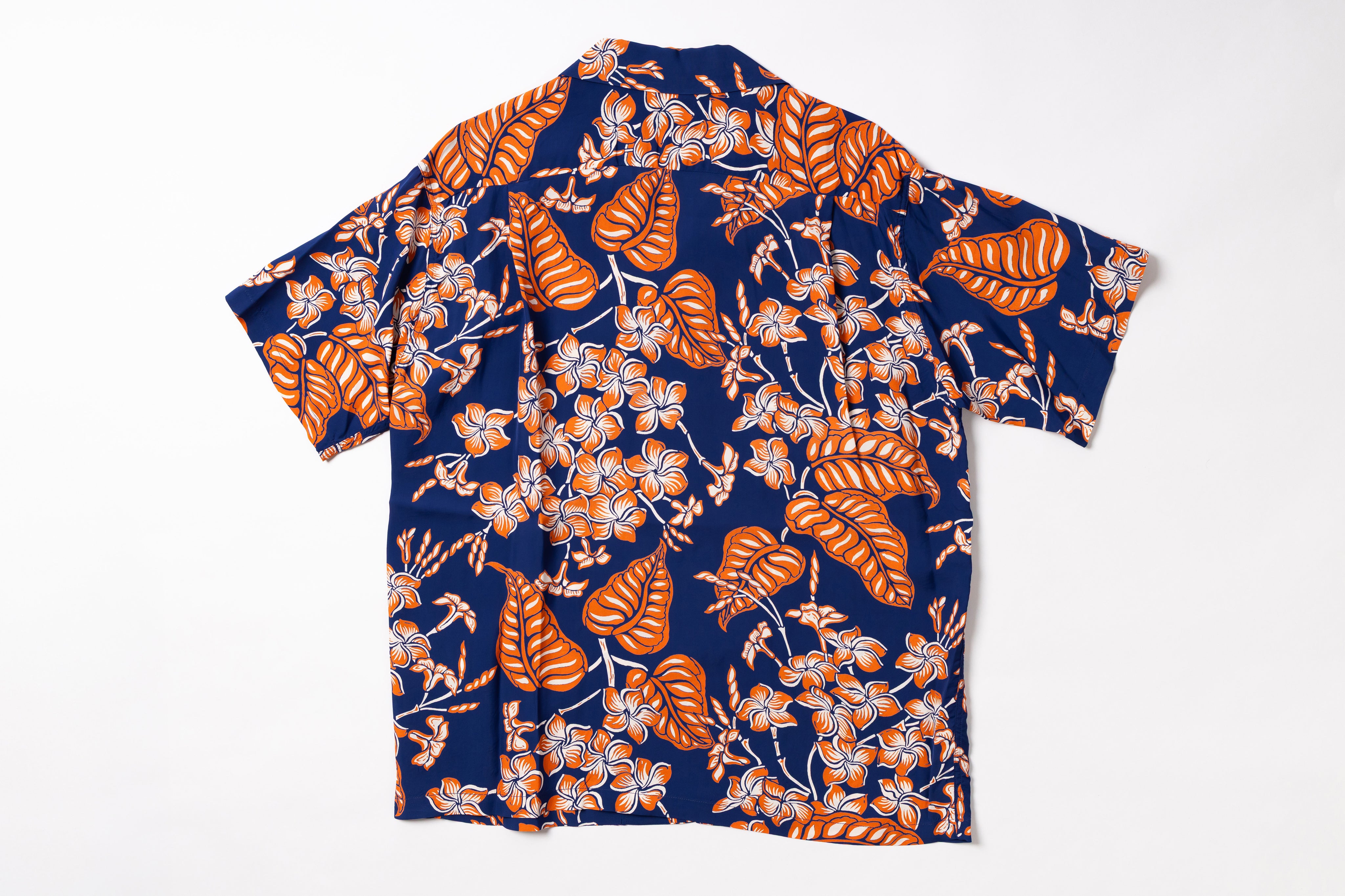 A short-sleeve button-up shirt laid flat on a white background, featuring a tropical floral and leaf print in orange, beige, and white over a dark navy blue base.