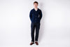 Man wearing a navy blue jacket and dark jeans standing against a white background