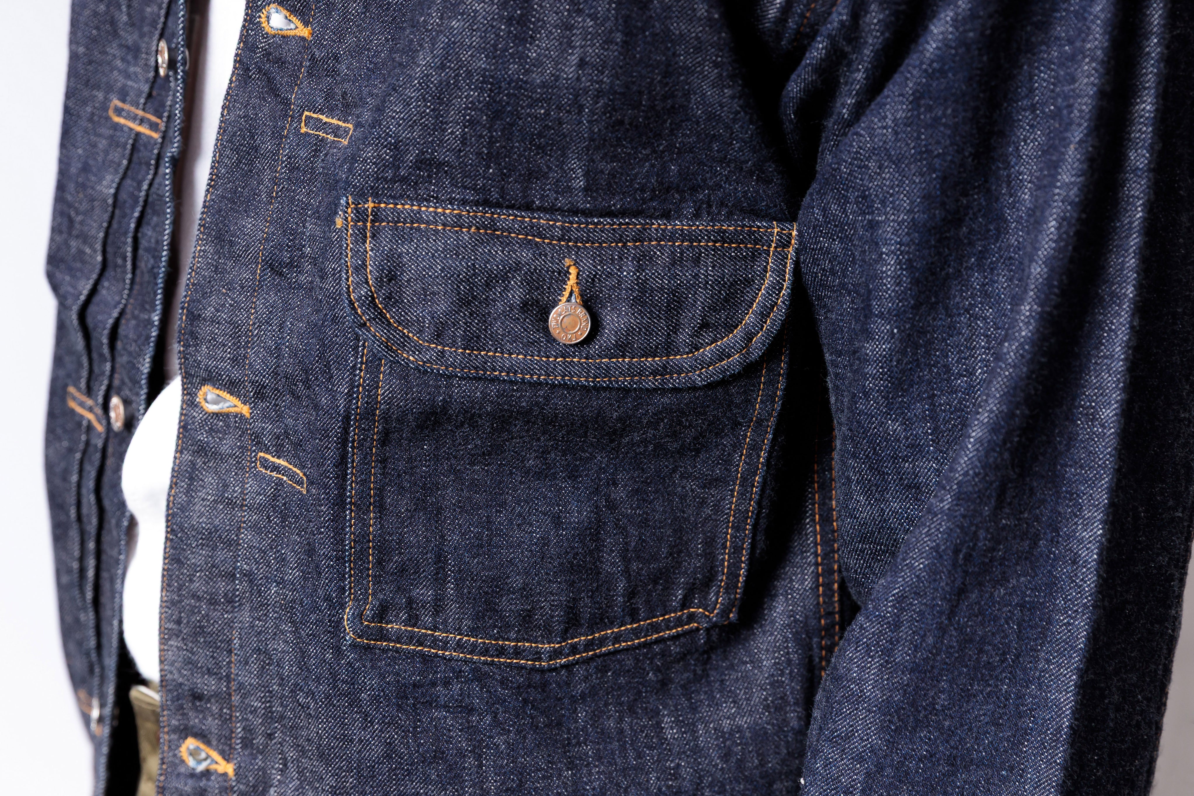 Close-up of a blue denim jacket with a pocket detail on a white background