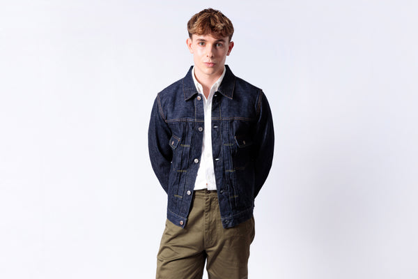 Man wearing a dark denim jacket over a white shirt with a light gray background