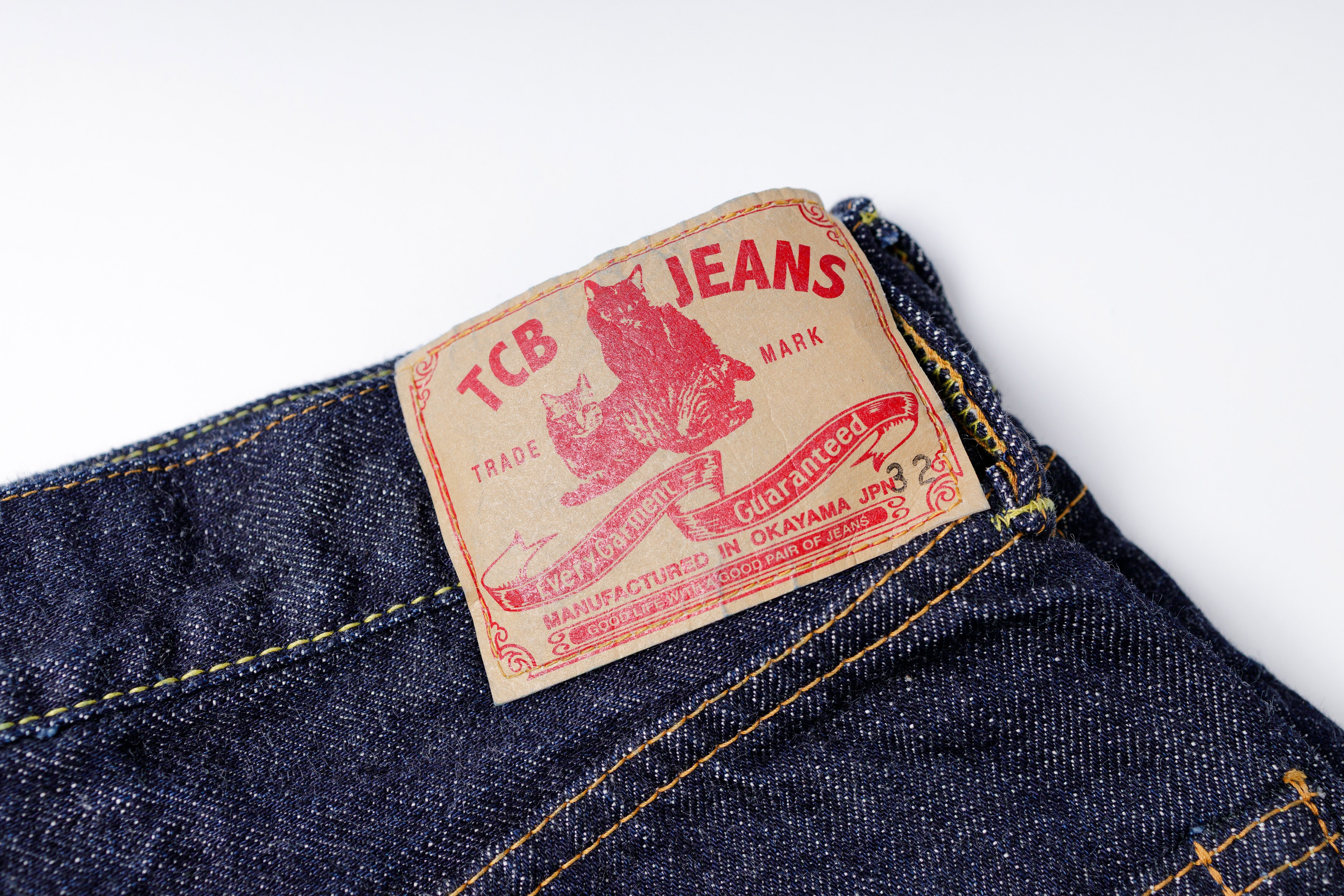 Close-up of a denim jeans label with 'TCB Jeans' branding on a white background