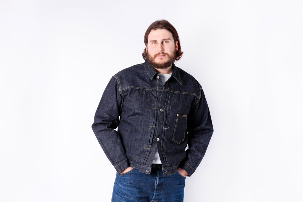 Man wearing a dark denim jacket and jeans on a white background
