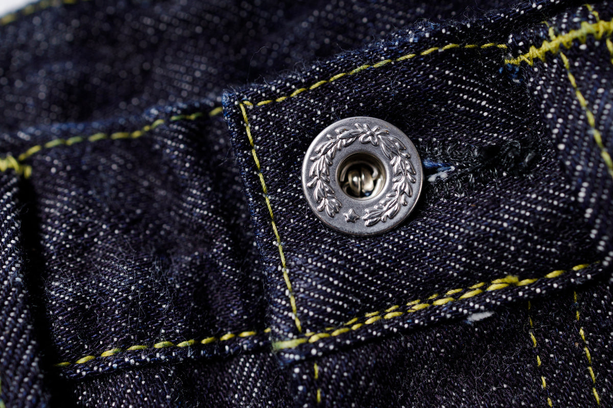 Close-up of a button on denim fabric with yellow stitching