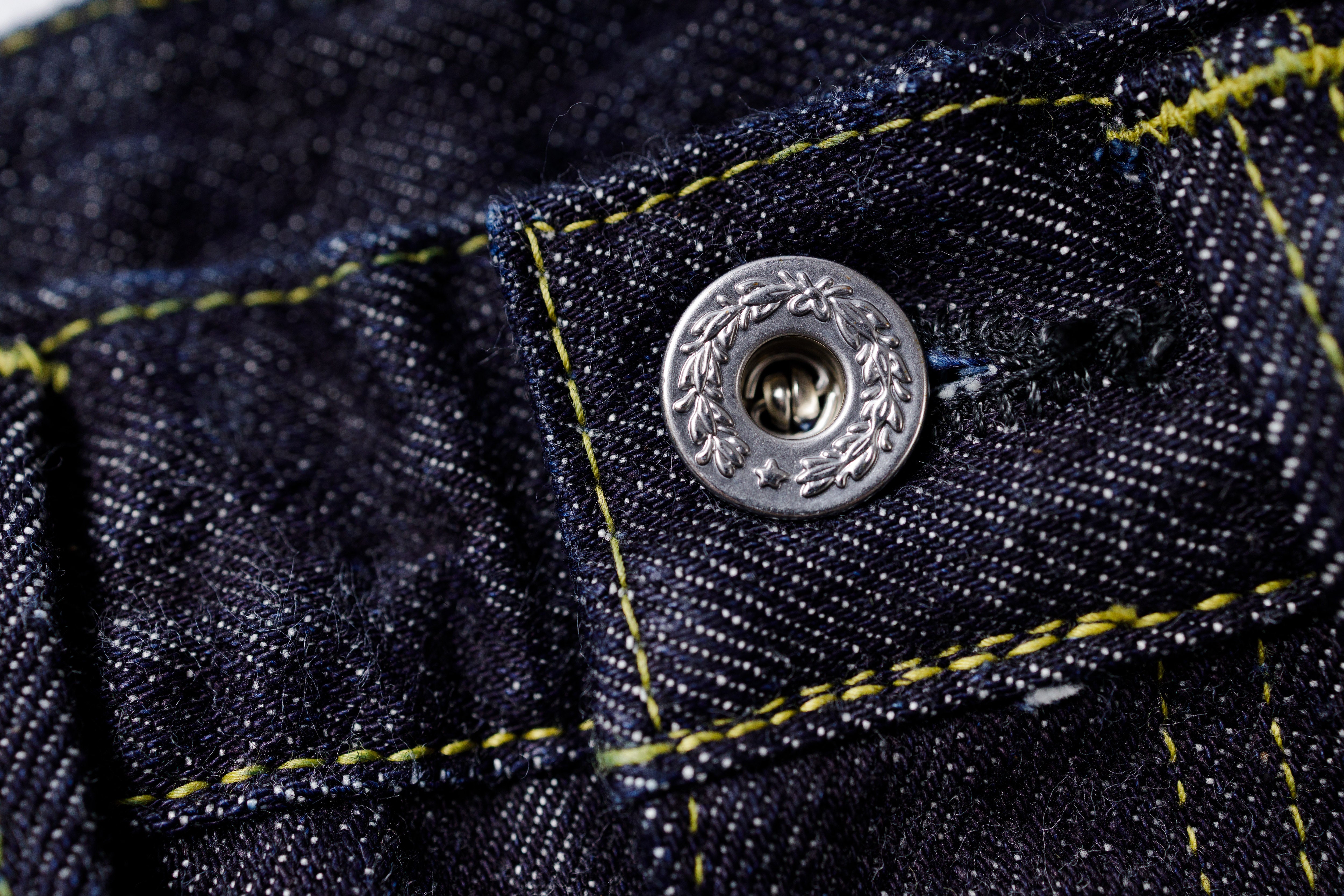 Close-up of a button on denim fabric with yellow stitching