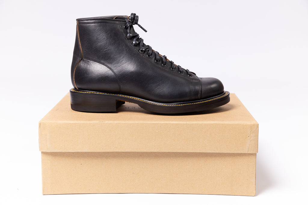 Black leather boot on a cardboard box against a white background